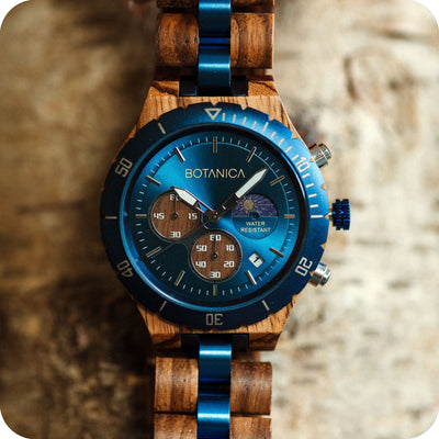 A blue faced watch with zebranowood links and casement sitting on a bark piece of wood