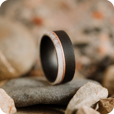 A Black Tungsten Steel ring with Deer antler bone resting on a collection of stones