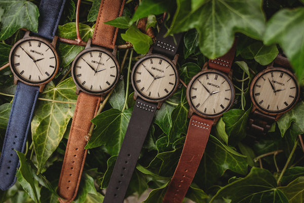 A collection of 5 wooden watches sitting on a bed of leaves