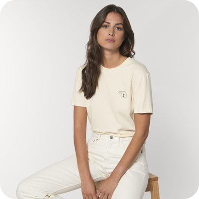 Women sitting on a chair with an off white organic cotton tee and bear logo inscription on the chest looking at the camera