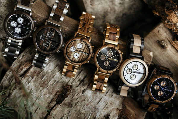 A collection of six wooden watches sitting on a log