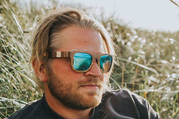 Man sitting in fields wearing wayfarer shape sunglasses with ice blue lens