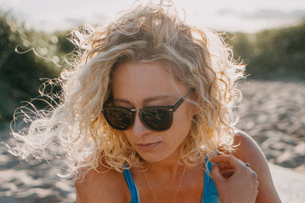 women holding hair on the beach wearing wooden sunglasses